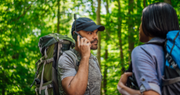 A backpacker makes a call using the Iridium satellite phone while in a remote forest while another backpacker stands next to him