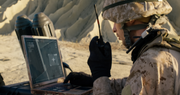 Soldier holding a satellite phone and looking at a laptop out in the field